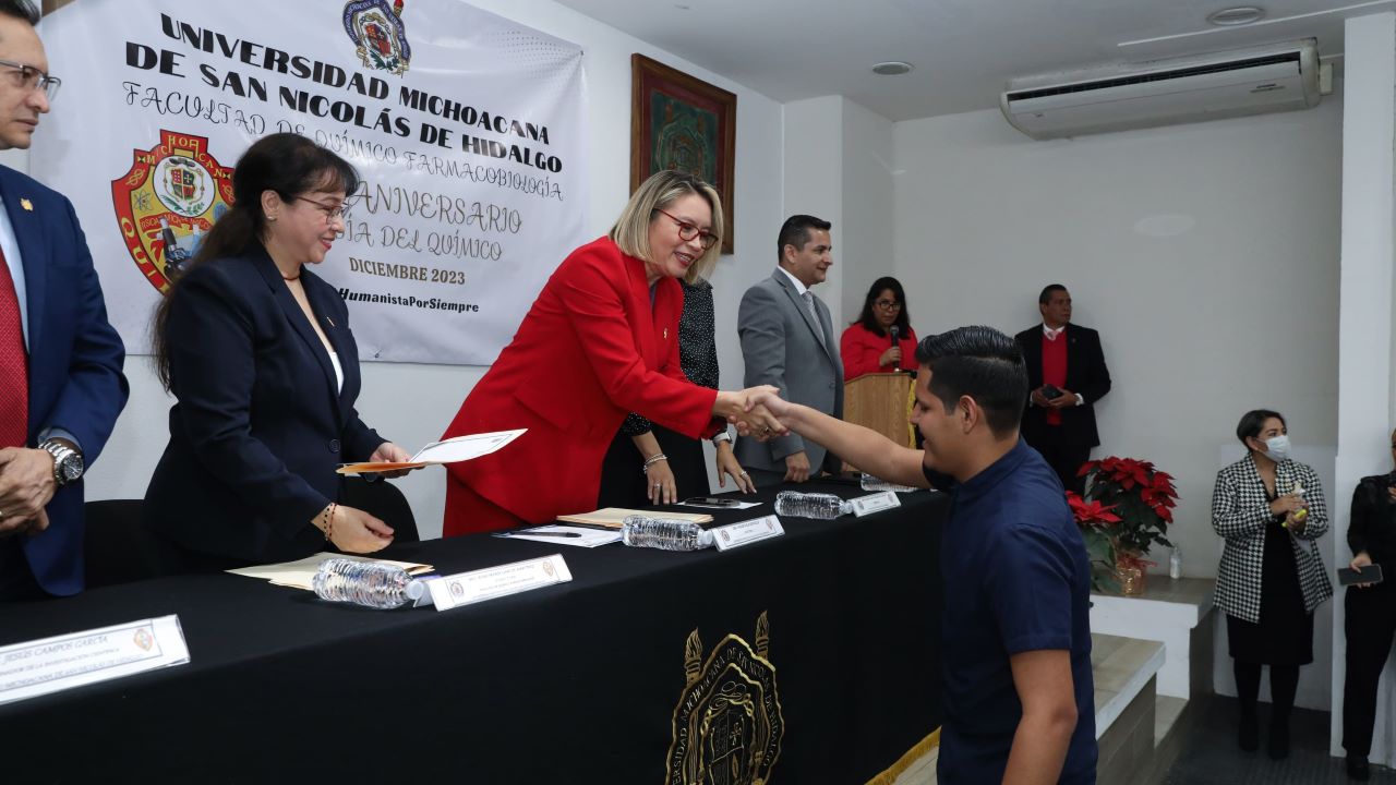 La rectora Yarabí Ávila González entregando un reconocimiento a un estudiante destacado de la UMSNH por sus excepcionales logros académicos en el 65° aniversario de la Facultad de Químico Farmacobiología