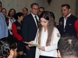 Una estudiante de Medicina recibe la documentación que oficializa su asignación al Internado Rotatorio, bajo la observación de autoridades universitarias y del sector salud.