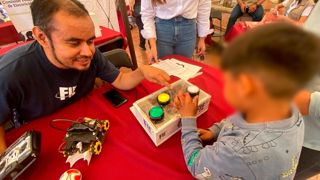 Un instructor de la Facultad de Ingeniería Eléctrica de la UMSNH guía a un niño en el manejo de un dispositivo de robótica durante el taller Robótica Kids, realizado en la localidad de Opopeo como parte de las Ferias Científicas del Plan Michoacán por la Paz y la Justicia. Un instructor de la Facultad de Ingeniería Eléctrica de la UMSNH guía a un niño en el manejo de un dispositivo de robótica durante el taller Robótica Kids, realizado en la localidad de Opopeo como parte de las Ferias Científicas del Plan Michoacán por la Paz y la Justicia.