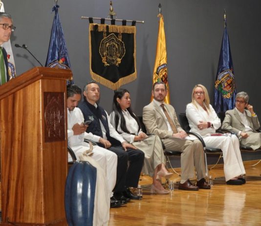 UMSNH celebra quince años de su Defensoría Universitaria Dr. Jesús Santillán, Intervención institucional en el estrado, acompañada de banderas y distintivos universitarios que subrayan el carácter formal de la ceremonia.