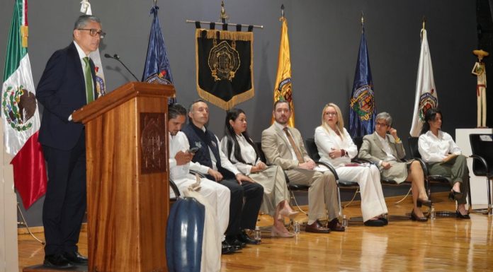 UMSNH celebra quince años de su Defensoría Universitaria Dr. Jesús Santillán, Intervención institucional en el estrado, acompañada de banderas y distintivos universitarios que subrayan el carácter formal de la ceremonia.