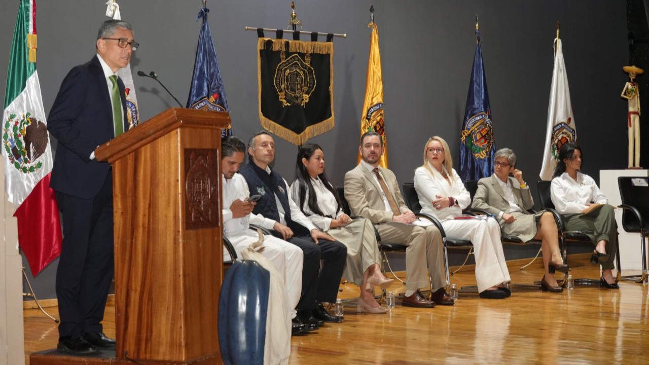 Dr. Jesús Santillán, Intervención institucional en el estrado, acompañada de banderas y distintivos universitarios que subrayan el carácter formal de la ceremonia. Dr. Jesús Santillán, Intervención institucional en el estrado, acompañada de banderas y distintivos universitarios que subrayan el carácter formal de la ceremonia.
