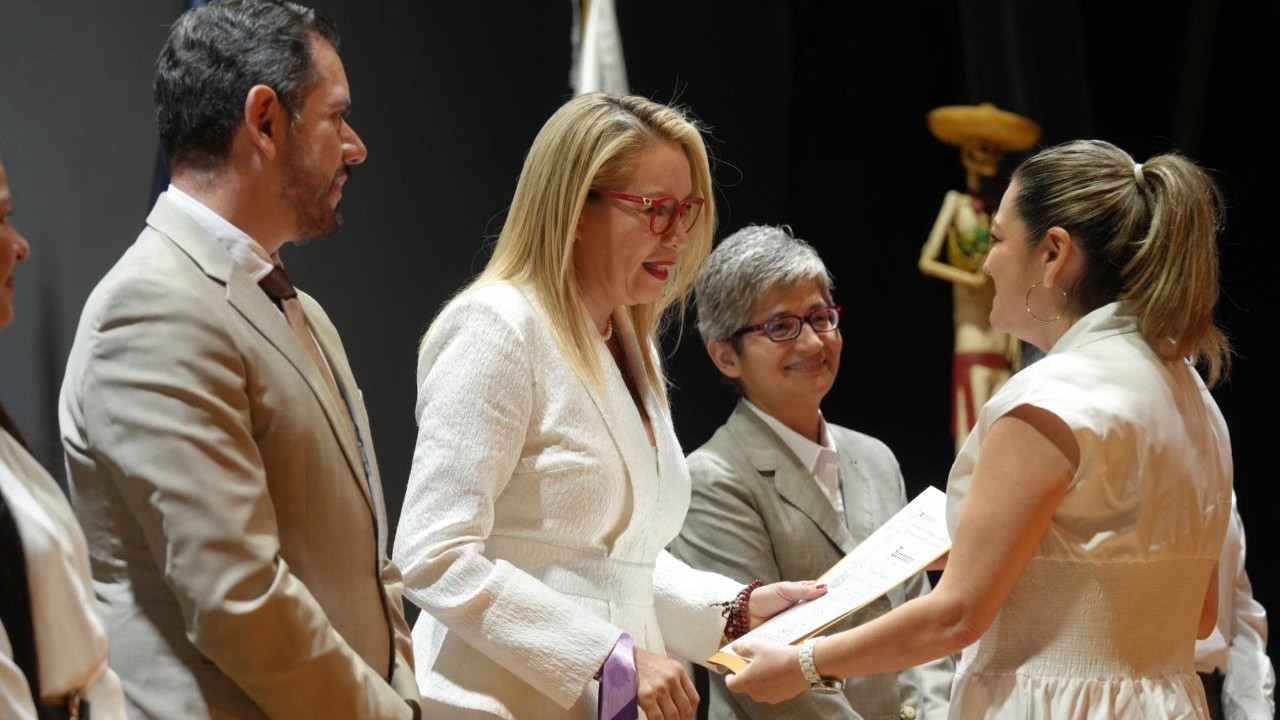 Autoridades universitarias realizan la entrega de un reconocimiento en el escenario, en un acto que resalta la labor institucional. Autoridades universitarias realizan la entrega de un reconocimiento en el escenario, en un acto que resalta la labor institucional.