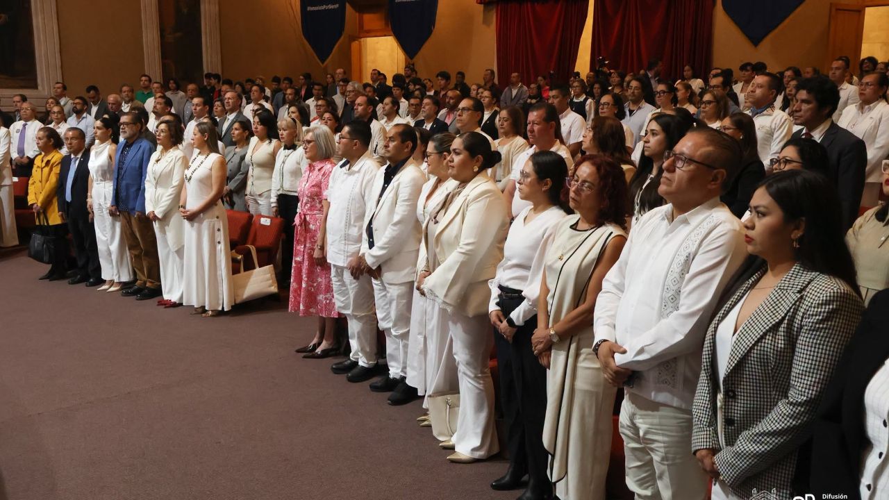 Asistentes reunidos en el auditorio participan en el acto conmemorativo, mostrando atención a las intervenciones oficiales. Asistentes reunidos en el auditorio participan en el acto conmemorativo, mostrando atención a las intervenciones oficiales.