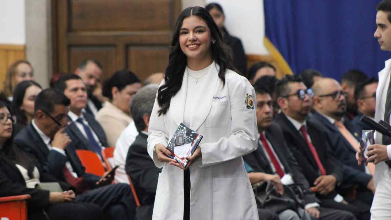 Itzel Andrea de la Cruz Mendoza, una de las estudiantes de la facultad de ciencias médicas que obtuvo el reconocimiento por su alto desempeño, portando su bata y el galardón en la ceremonia de la UMSNH. Itzel Andrea de la Cruz Mendoza, una de las estudiantes de la facultad de ciencias médicas que obtuvo el reconocimiento por su alto desempeño, portando su bata y el galardón en la ceremonia de la UMSNH.